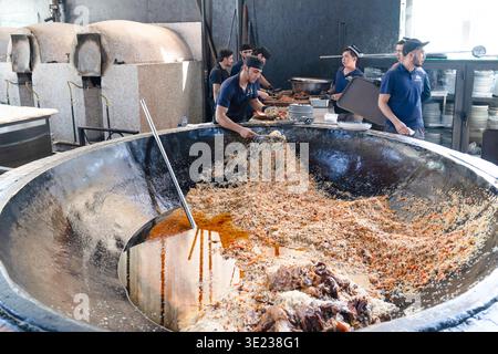 Tashkent (Toshkent), Uzbekistan (o'zbekiston) - 26 maggio 2025: Gli chef servono plov tradizionale uzbeko da un enorme calderone in ghisa al Besh Qozon ( Foto Stock