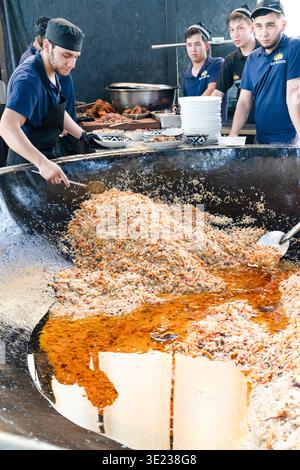 Tashkent (Toshkent), Uzbekistan (o'zbekiston) - 26 maggio 2025: Vista verticale degli chef serve plov tradizionale uzbeko da un enorme calderone in ghisa a. Foto Stock