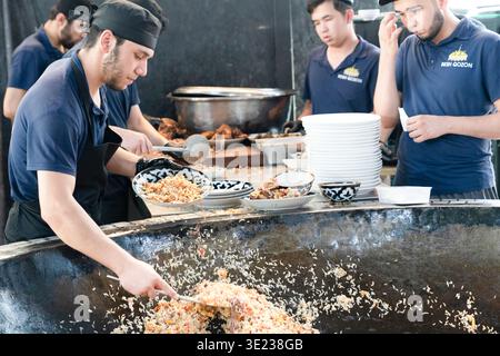 Tashkent (Toshkent), Uzbekistan (o'zbekiston) - 26 maggio 2025: Vista ravvicinata degli chef serve plov tradizionale uzbeko da un enorme calderone in ghisa a. Foto Stock