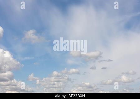 Le nuvole bianche di cumulus attraversano il cielo azzurro il paesaggio calmo e suggestivo lo sfondo del clima sereno. La luce solare soffusa illumina le forme delle nuvole Foto Stock