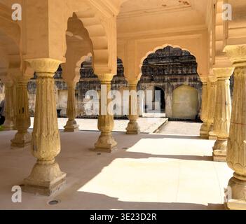 Cortile illuminato dal sole con colonne in pietra scolpita e archi smerlati all'interno del forte Amber a Jaipur. Architettura storica del palazzo indiano che enfatizza la simmetria, Foto Stock