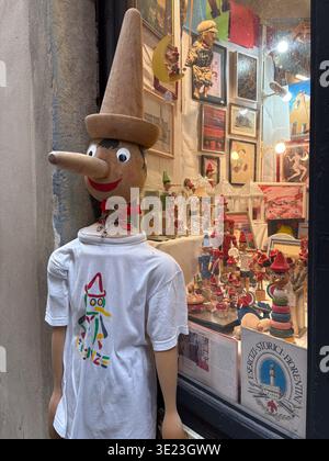 Il manichino di bambola Pinocchio in legno espone la camicia vicino alla vetrina piena di statuette in legno e opere d'arte. Firenze, Italia. Foto Stock