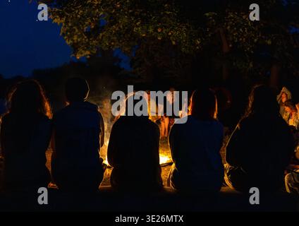 Gruppo di persone che si radunano intorno al falò di notte Foto Stock