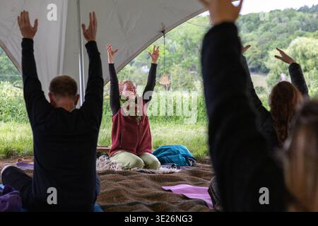 Adulti che alzano le braccia durante una piacevole sessione di yoga all'aperto sotto una tenda Foto Stock