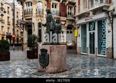Monumento al Procesionista a Cartagena, Spagna, con statue in bronzo dei penitenti pasquali su una base in marmo in una piazza urbana lastricata. Foto Stock