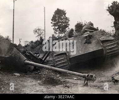 Due soldati americani che esaminano il relitto di un carro armato tedesco Panther. Il carro è stato distrutto da un'esplosione abbastanza violenta da far esplodere completamente la torretta. Il 6 giugno 1944 un'enorme forza di invasione Alllied, che coinvolgeva 7000 navi e 140.000 uomini, sbarcò con successo sulla costa francese e stabilì cinque teste da spiaggia. Una campagna di inganno di successo significò che gran parte della resistenza tedesca si trovava a Calais e le perdite furono relativamente poche per le dimensioni e i rischi dell'operazione. Foto Stock