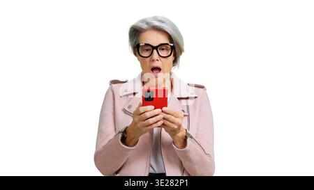 Donna anziana che reagisce con sorpresa utilizzando uno smartphone rosso Foto Stock