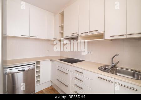 Cucina moderna con armadi bianchi, elettrodomestici in acciaio inox e un piano di lavoro pulito. Lo spazio è luminoso e minimalista, ideale per cucinare e. Foto Stock