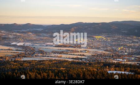 Una vista di Liberec durante una mattina d'inverno. Il paesaggio mostra montagne sullo sfondo e campi ricoperti di neve. La città è parzialmente visibile con edifici e alberi in primo piano. Foto Stock