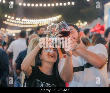 Al festival Yerevan Wine Days, due visitatori reggono bicchieri da vino rosso e bianco per una foto in mezzo alla folla. Foto Stock