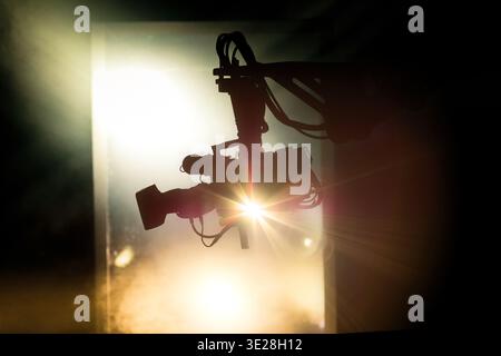 Silhouette di una videocamera professionale su una gru con luce parassita e fumo in uno sfondo cinematografico Foto Stock