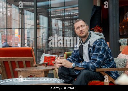 L'uomo siede in un lounge moderno con pareti di vetro e tavoli rustici in legno Foto Stock