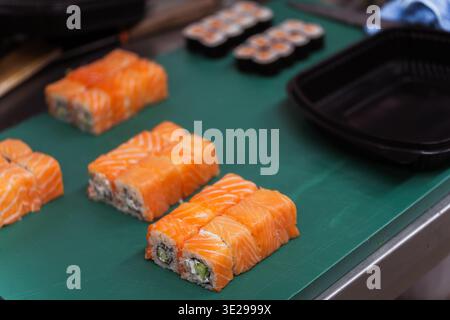 Sushi al salmone fresco su tappetino verde con bancone della cucina e area di preparazione sfocata, assemblaggio dello chef Foto Stock