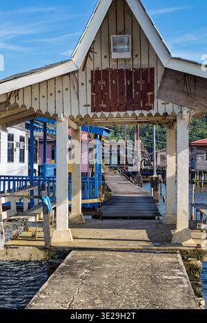 Ammira attraverso un tradizionale arco in legno e passerella le vivaci case palafitte di Kampong Ayer, Bandar seri Begawan, Brunei, sotto un cielo blu brillante Foto Stock