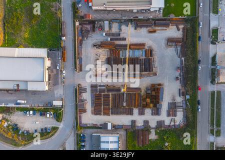 Veduta aerea di un deposito pieno di banchi di metallo e di una gru gialla, in contrasto con il paesaggio urbano circostante, vasto, Abruzzo Foto Stock