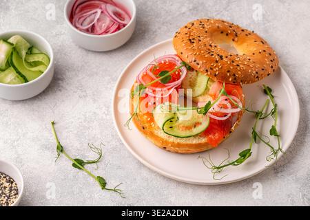 Bagel e losco di salmone con formaggio cremoso, cetrioli, cipolle e microgreens. Foto Stock