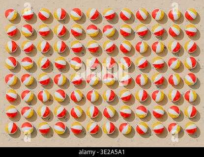 Rendering 3D delle palle da spiaggia gonfiabili disposte in una griglia a ripetizione ordinata su una superficie sabbiosa testurizzata. Le sfere lucide con colori alternati Foto Stock
