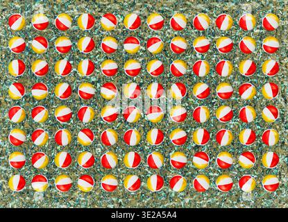 Rendering 3D di un modello ripetuto di palline da spiaggia gonfiabili disposte in una griglia regolare sopra una superficie d'acqua testurizzata. Foto Stock