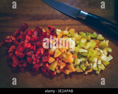 Peperoni colorati a dadini in file sfumate su un tagliere in legno Foto Stock