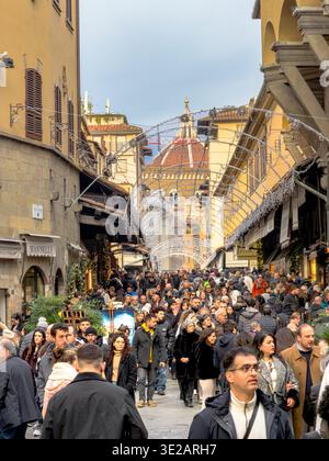 Folle di persone che camminano attraverso il Ponte Vecchio, un ponte medievale ad arco in pietra sul fiume Arno, a Firenze, Italia Foto Stock