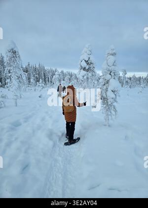 Una persona in un'avventura con racchette da neve ad Akaslompolo, Lapponia, circondata da splendidi alberi innevati. Il tranquillo paesaggio offre una magica atmosfera invernale perfetta da esplorare. Foto Stock