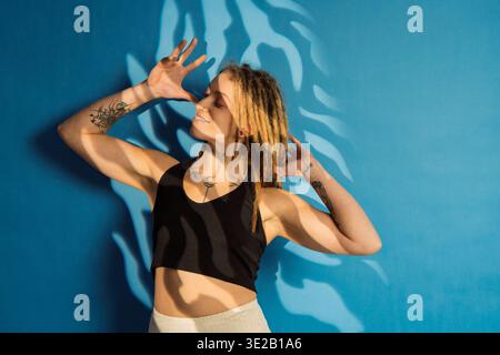Giovane donna che posa con dreadlock e tatuaggi, godendosi il sole e le ombre delle foglie Foto Stock