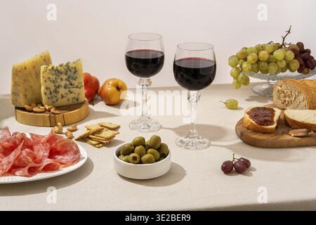 Calici di vino rosso con uva, formaggio e salumi su fondo da tavola chiaro. Vino rosso con formaggio e frutta. Spazio per il testo Foto Stock