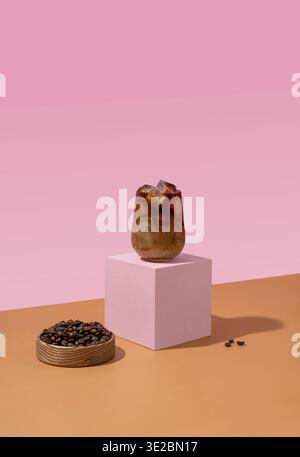 Ghiacciare il caffè in un bicchiere alto con la panna versata sopra e i chicchi di caffè su sfondo rosa Foto Stock