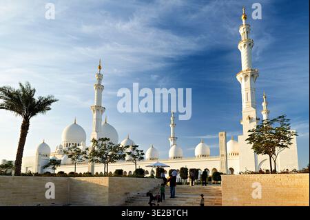 La gente cammina vicino alla splendida architettura della grande Moschea dello sceicco Zayed ad Abu Dhabi. Il cielo è limpido e blu durante il giorno. Foto Stock