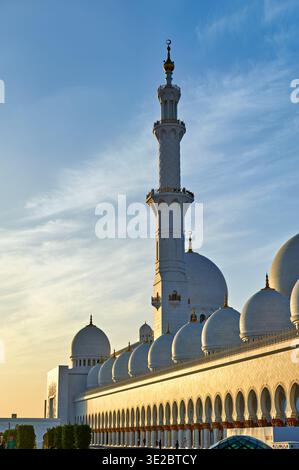 I visitatori ammirano la grande Moschea dello sceicco Zayed ad Abu Dhabi mentre il sole tramonta. L'architettura mostra grandi dettagli e design sotto il cielo serale. Foto Stock