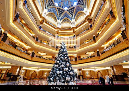Le persone camminano intorno alla lobby dell'Emirates Palace Hotel ad Abu Dhabi. Al centro sorge un grande albero di Natale, decorato con luci. Foto Stock