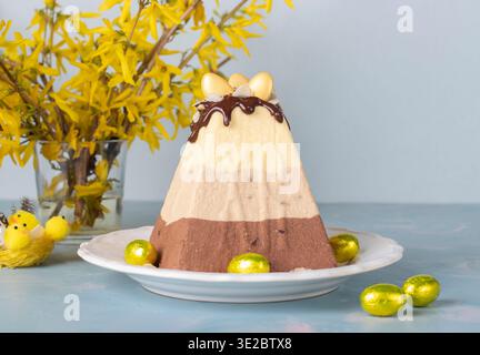 Tradizionale dessert di Pasqua a base di cagliata composta da tre tipi di cioccolato: Bianco, latte e nero, decorato con uova di cioccolato su sfondo blu Foto Stock