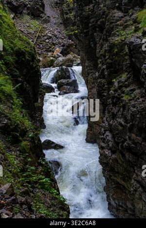 Un potente torrente di montagna scorre attraverso una stretta gola rocciosa, che si getta su massi e crea acque bianche spumeggianti. Pareti rocciose ripide incorniciano il tu Foto Stock