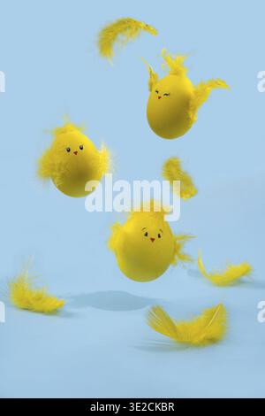 Graziose uova di Pasqua gialle a forma di pulcini circondate da piume su uno sfondo blu brillante. Biglietto da regalo di Pasqua Foto Stock