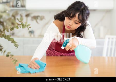 La casalinga pulisce la superficie del tavolo con lo straccio nella cucina moderna Foto Stock