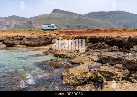 Vista di un camper bianco parcheggiato sulle scogliere di Cala Calazza, Macari. Cattura la bellezza selvaggia della costa siciliana con il monte cofano sul retro Foto Stock