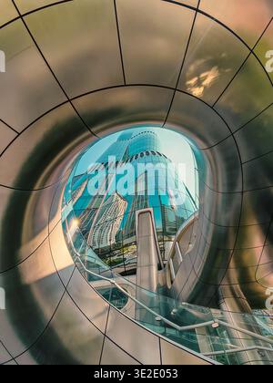 18 marzo 2026 - Hong Kong: Una sorprendente immagine ad alta risoluzione che mostra un elegante edificio contemporaneo riflesso all'interno di un tunnel di vetro curvo nel centro di H. Foto Stock
