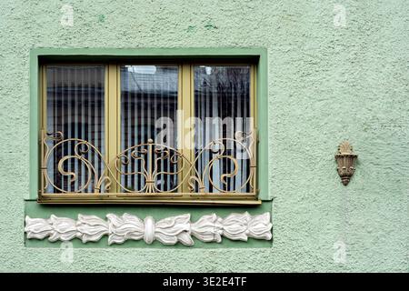 Finestra rettangolare con telaio giallo e griglia aperta con modanature bianche contro una parete verde. Dalla serie di finestre di San Petersb Foto Stock