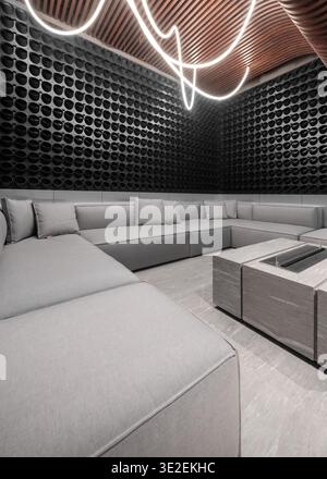 Salotto con divano grigio e illuminazione a tubo curvo. Interni lounge con divano modulare grigio, tavolo minimalista per caminetto e lampada al neon curva, Foto Stock