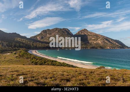 Una tranquilla scena costiera caratterizzata da una spiaggia sabbiosa, una baia turchese e aspre montagne a Freycinet. Foto Stock