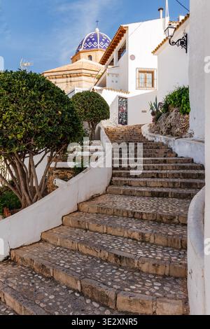 Scale in pietra nel centro storico con la cupola della chiesa di Nuestra Senora del Consuelo sullo sfondo ad Altea il 19 marzo 2026, Spagna Foto Stock