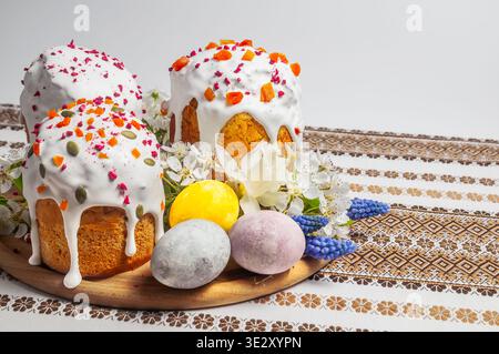 Uno shot ravvicinato mostra tre torte pasquali splendidamente decorate, adornate con glassa bianca, frutta secca e semi, insieme a uova colorate dipinte Foto Stock