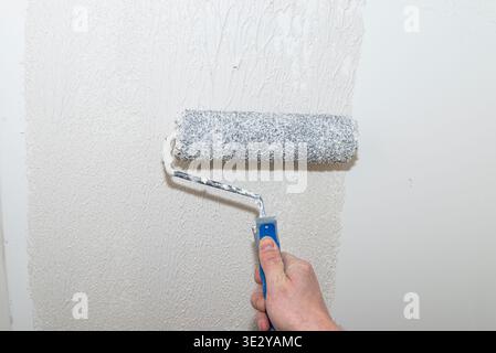 Utilizzare a mano un rullo per applicare uno spesso strato di intonaco polimerico ruvido su una parete durante la ristrutturazione Foto Stock