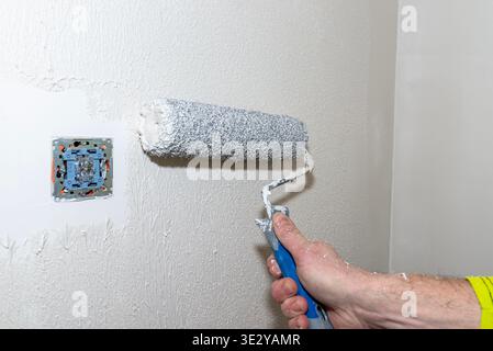 Applicazione manuale di uno strato spesso di intonaco polimerico a una parete con un rullo durante la ristrutturazione Foto Stock