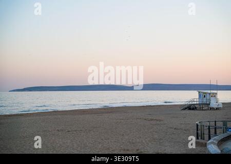 Spiaggia vuota di Bournemouth al tramonto con torre bagnino, mare calmo e cielo color rosa pastello al tramonto sulla costa del Dorset, Inghilterra Regno Unito Foto Stock