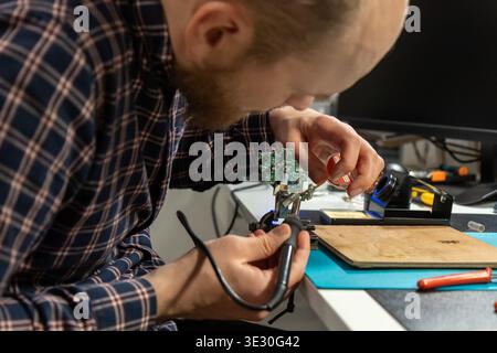 Un'immagine dettagliata cattura un uomo che ripara diligentemente una complessa scheda di circuito verde, tenuta saldamente in una morsa, mentre manipola con precisione Foto Stock