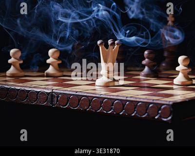 Un primo piano di una foto concettuale di fumo che si libra su una scacchiera con alcuni pezzi di scacchi. Foto Stock