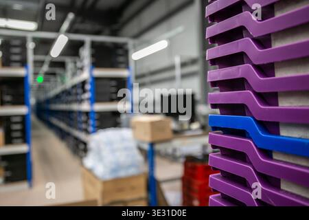 All'interno di un magazzino logistico con casse in plastica viola impilate in primo piano e lunghe corsie di scaffalature riempite di inventario sul retro Foto Stock