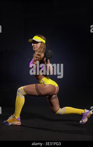 Giovane donna che indossa un abbigliamento sportivo colorato, che fa esercizi di forza per le gambe in palestra. Stile di vita fitness. Foto Stock