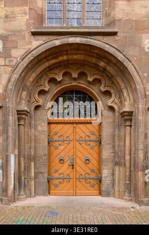 Porta storica ad arco con cornice in pietra ornata e doppie porte in legno arancione brillante con elementi decorativi in ferro Foto Stock